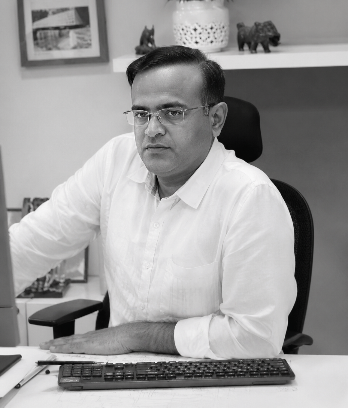 Professional man in a white shirt and glasses seated at a desk in an office, facing the camera
