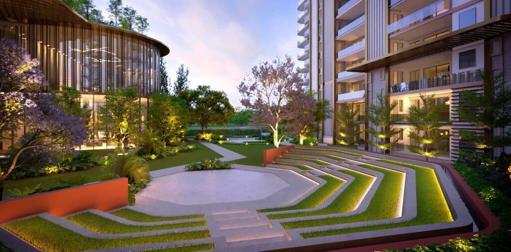 Night-time view of a modern apartment courtyard with glass-walled common area, curved lines, and illuminated landscaping between buildings.
